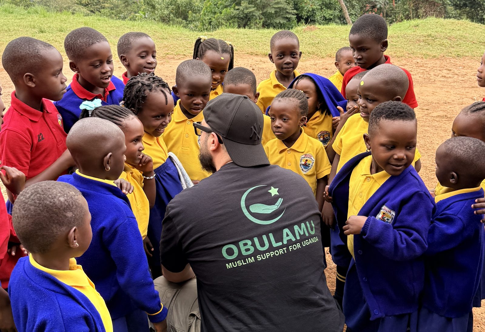Besuch an einer Schule in Uganda: ein Helfer von Obulamu kniet zwischen Schulkindern